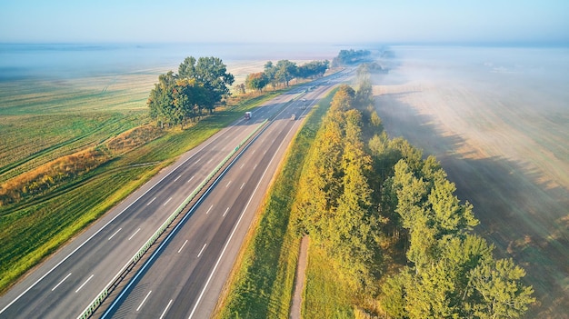 Zonnige magische herfst mistige ochtend. Luchtfoto van snelweg met auto's. Asfaltweg bedekt met mist. Vroege mistige dageraad. M1 magistraal in Wit-Rusland