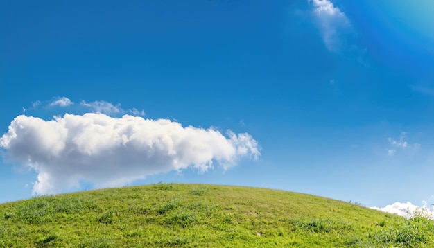 Zonnige natuurlijke zomerachtergrond met met gras begroeide ronde heuvel en heldere blauwe lucht