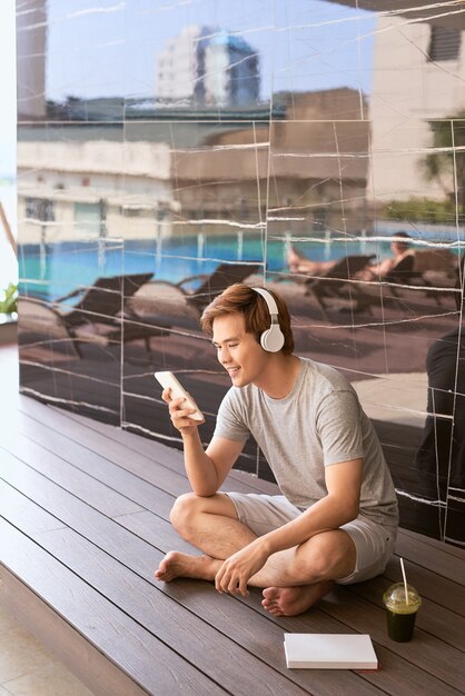Zonnige zomerdag, vrolijke aantrekkelijke glimlach aziatische man gebruikt de smartphone