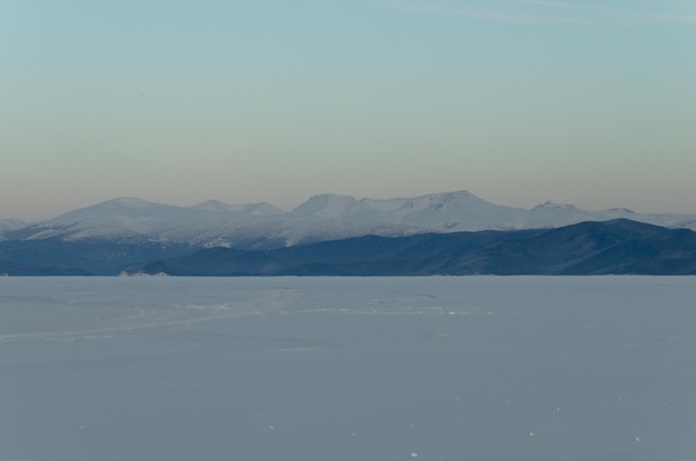 Zonsondergang aan de oever van een bevroren meer Een eindeloos veld van sneeuw en bergen in de verte