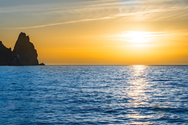 Zonsondergang boven de blauwe zee met rotsen en oranje lucht