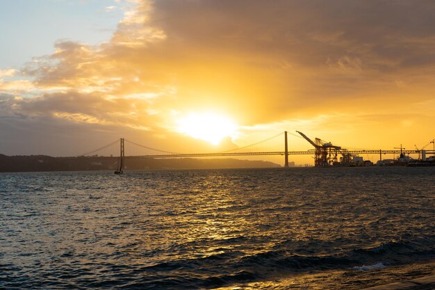 Zonsondergang boven de zee en silhouetten van een brug en een industriële kraan