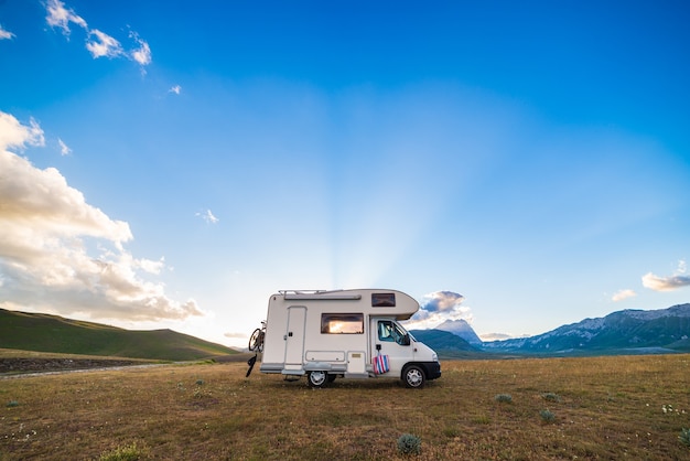 Zonsondergang dramatische hemel boven kampeerauto in Campo Imperatore hooglanden, Abruzzo, Italië. Epische wolken boven unieke hooglanden en rotsachtig berglandschap, alternatief vanlife-vakantieconcept.