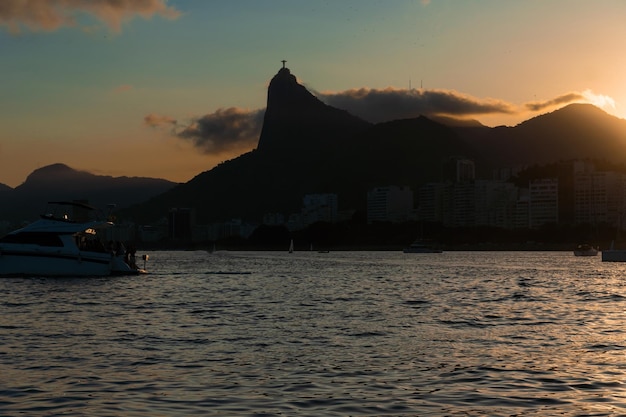 Zonsondergang in de baai van guanabara inham en stranden van rio de janeiro brazilië met zijn gebouwen boten en landschap christus de verlosser bovenop corcovado reflectie van de lucht in de zee