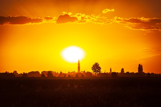 Zonsondergang in een landschap met klokkentoren, bomen en landschap