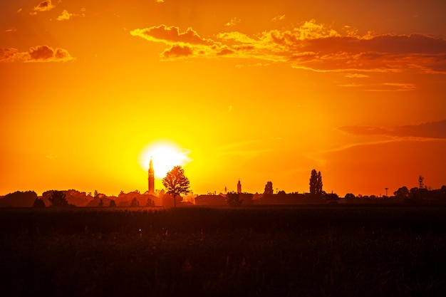 Zonsondergang in een landschap met klokkentoren, bomen en landschap