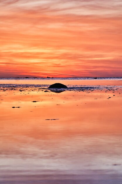 Zonsondergang kleine rots bij eb voor de verlichte zee Lichtgolven