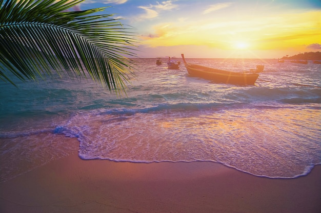 Zonsondergang met lang verhaalboot op kleurrijk overzees strand en blauwe hemel