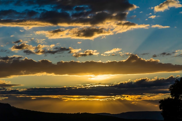 Zonsondergang op een dag met wolken en zonnestralen die eruit komen in de berg.