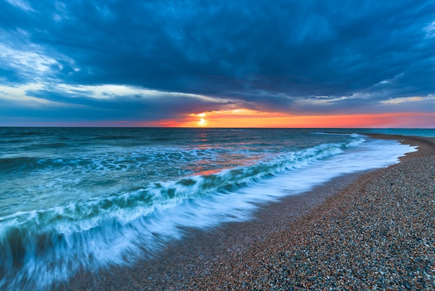 Zonsondergang op het strand met lange kustlijn, zon en dramatische hemel