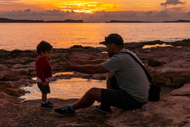 Zonsondergang op Ibiza op vakantie jonge vader met zijn zoon aan zee in San Antonio Abad