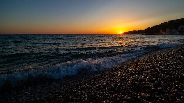 Zonsondergang op zee. Kiezelstrand, golven