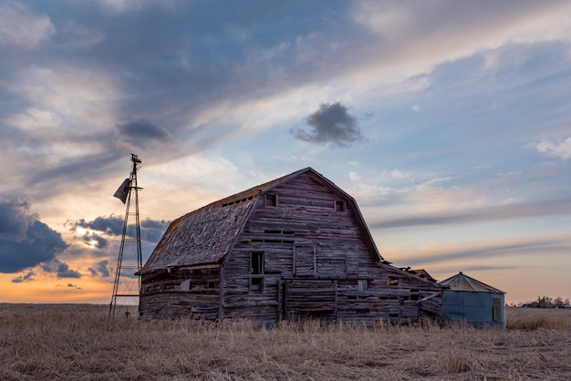 Zonsondergang over een vintage houten schuur, bakken en windmolen in een Saskatchewan, Canada