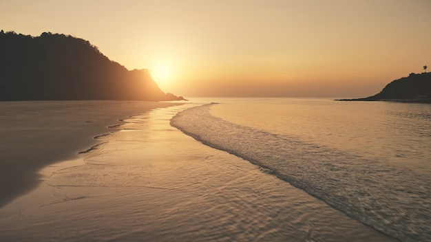 Zonsondergang over oceaangolven wassen zandstrand. Luchtfoto zonsondergang boven berg silhouet. Tropic niemand