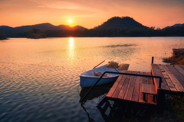 Zonsondergang schijnt over berg en meer met boot op houten pier in landelijke scène