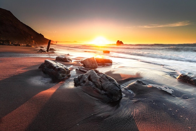 Foto zonsondergang terwijl zeegolven de rotsen raken op het strand van het strand van ilbarritz in biarritz, baskenland