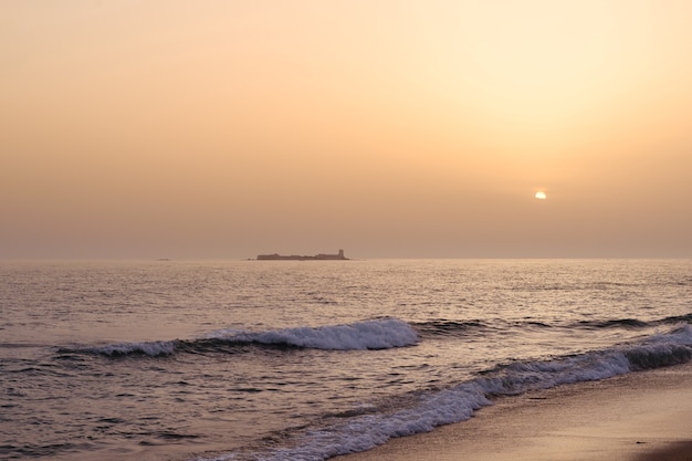 Zonsonderganglandschap van het strand en de zee met een kasteel op de achtergrond