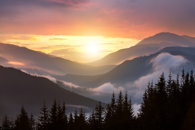 Zonsonderganglandschap van hoge bergtoppen en mistige vallei onder levendige kleurrijke avondlucht.