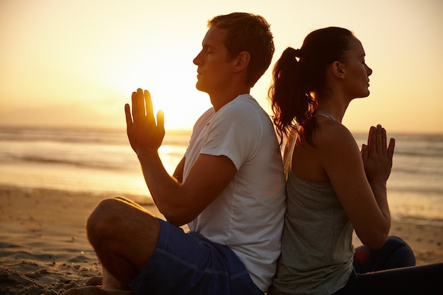 Zonsondergangmeditaties Shot van een stel dat mediteert op het strand bij zonsondergang