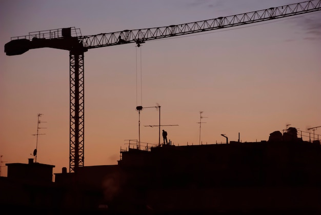 Zonsondergangmening van een dak met silhouet van een arbeider en een bouwkraan