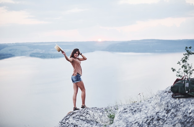 Zonsondergangstemming. Aantrekkelijk toeristenmeisje poseren aan de rand van de berg met helder watermeer op achtergrond.