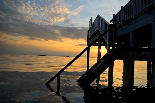 Zonsopgang op het eiland van de Maldiven met de toevlucht van de watervilla en weerspiegeling van zonlicht op overzees.