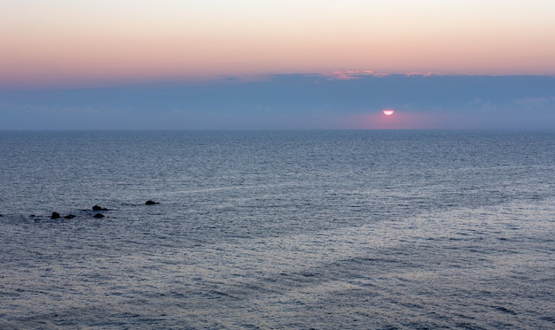 Zonsopgang zee landschap met zon in de lucht en toppen van onderwater rotsen boven water.