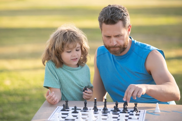 Zoon die op gras ligt en schaak speelt met vader Geconcentreerde jongen die een schaakstrategie ontwikkelt en een bordspel speelt met de ouder Games en activiteiten voor kinderen