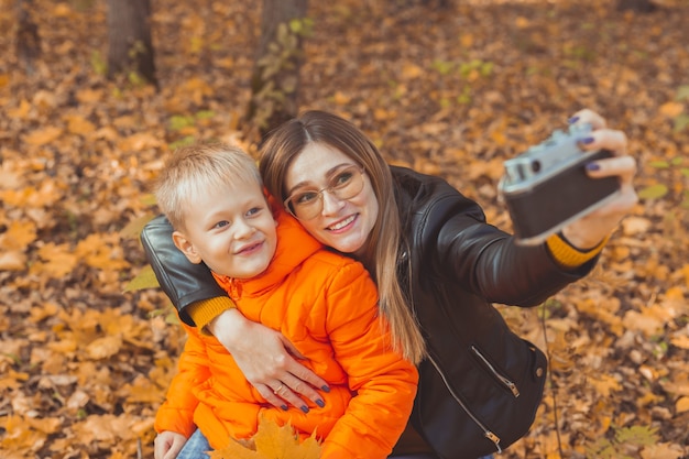 Zoon en moeder nemen selfie op camera in herfstpark, vrije tijd voor alleenstaande ouders en herfstseizoen