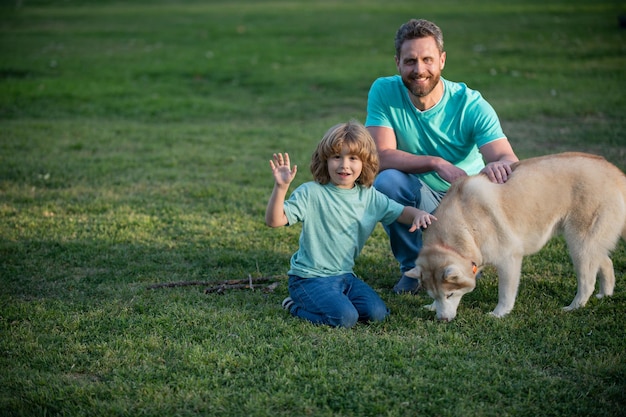 Zoon en vader als gezin met hond die samen spelen in het zomerpark op graskind met haar huisdiervriend