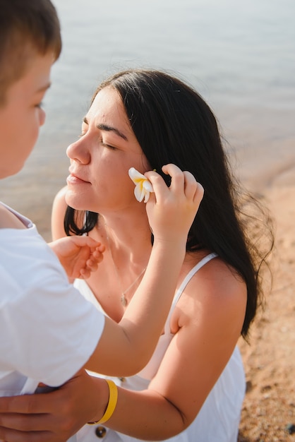 Zoon zet een bloem in het haar van zijn moeder aan het strand