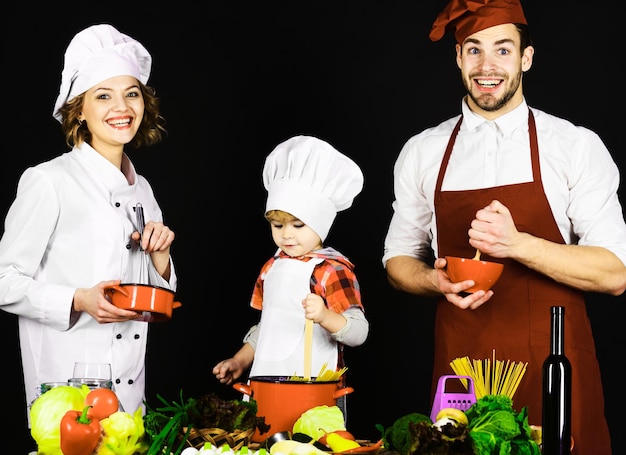 Zoontje met ouders koken in de keuken samen zelfgemaakte gerechten gelukkige familie in chef-kok uniform