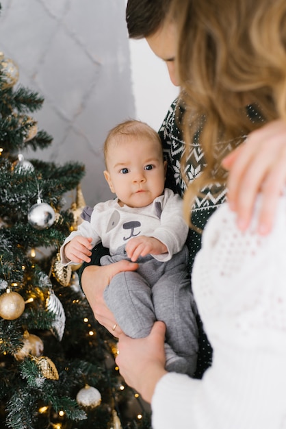 Zoontje van vijf maanden in zijn ouders armen dicht bij een kerstboom