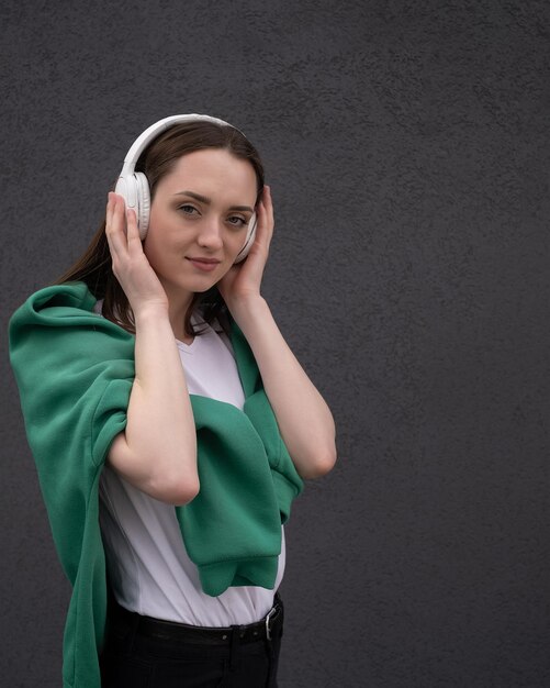 Zorgeloos aantrekkelijk brunette meisje gekleed in een grijze trui luisteren naar muziek koptelefoon staan