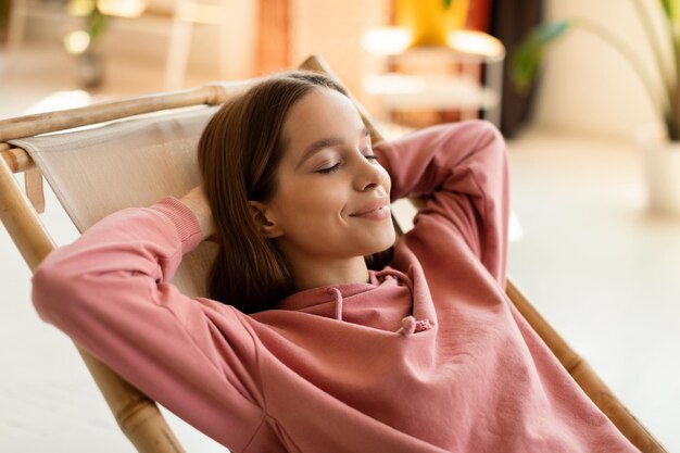 Foto zorgeloos gelukkig tienermeisje ontspannen in de stoel met handen achter haar hoofd tijd thuis doorbrengen na studies