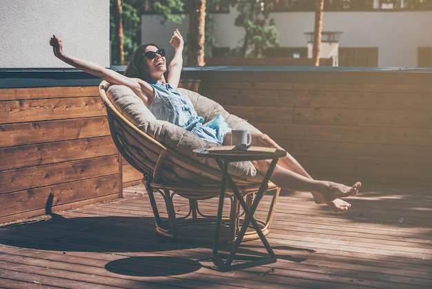 Zorgeloos genieten. mooie jonge vrouw ontspannen in een grote comfortabele stoel op haar buitenhuisterras