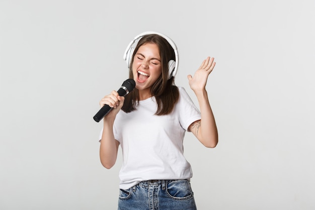Zorgeloos glimlachend meisje karaoke spelen, zingen in microfoon met koptelefoon.