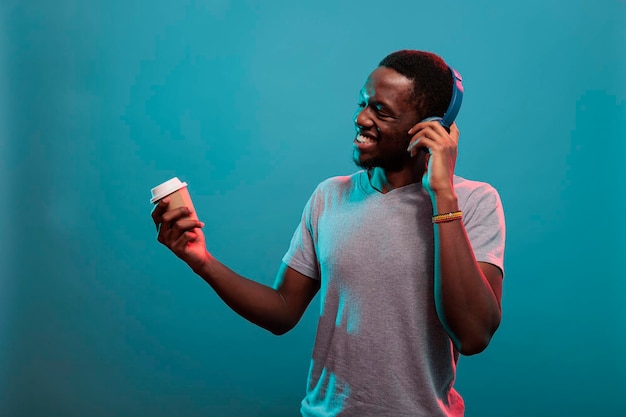 Zorgeloos persoon die geniet van mp3-muziek op een koptelefoon en een kopje koffie, luisterend naar het opnemen van een nummer op een draadloze headset. gelukkig model dat moderne audiogadgets gebruikt om plezier te hebben, drinken vast te houden.