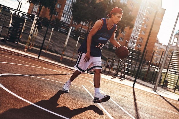 Zorgeloos spel. Volledige lengte van jonge man in sportkleding die basketbal speelt terwijl hij buiten tijd doorbrengt