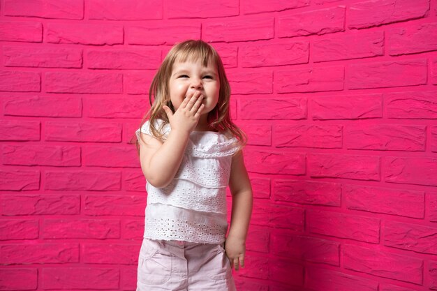 Zorgeloos vrolijk meisje hardop lachen giechelend voor haar mond met haar hand op roze oppervlak.