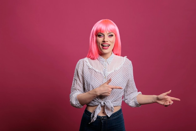 Zorgeloze gelukkige volwassene met roze haar zijwaarts wijzend in de studio, met vermelding van links of rechts richtingen voor de camera. Op die manier aanbevelen met opgeheven armen en wijsvingers.