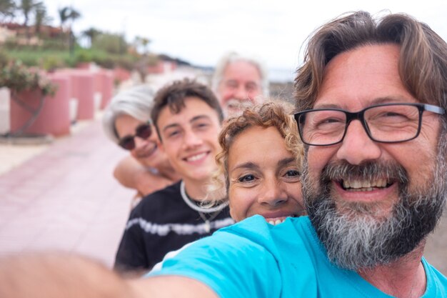 Zorgeloze groep van meerdere generaties familie die een selfie buiten op het strand maakt, glimlachend naar de camera kijkend