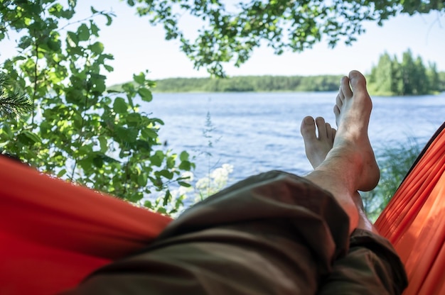 Zorgeloze man op blote voeten ontspant liggend in een hangmat in de schaduw van bomen met een prachtig uitzicht op het meer