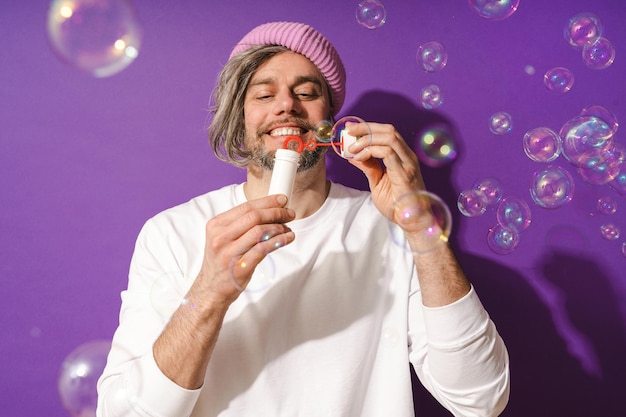 Zorgeloze man van middelbare leeftijd die zeepbellen blaast op een paarse achtergrond