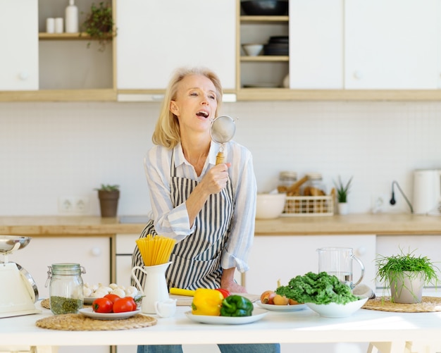 Zorgeloze senior vrouw die plezier heeft tijdens het koken in een lichte moderne keuken thuis at