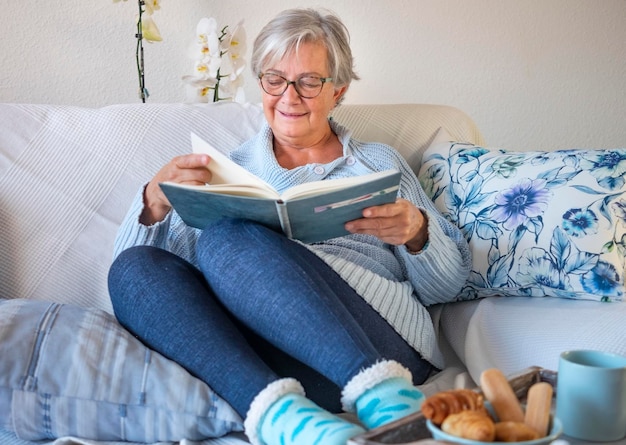 Zorgeloze senior vrouw schrijven op een notitieboekje ontspannen op de bank voor een pauze met eten en drinken volwassen ouderen genieten van pensioen