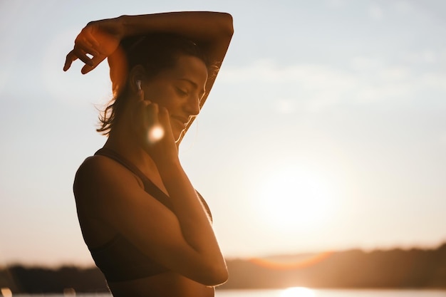 Zorgeloze sportvrouw genieten in de vroege ochtendzon terwijl ze naar muziek luistert via oortelefoons in de natuur Ruimte kopiëren