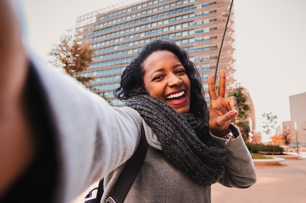 Zorgeloze vrouw die naar de camera kijkt en glimlacht terwijl ze een selfie neemt en buitenshuis een vredesteken toont Lifestyle Concept