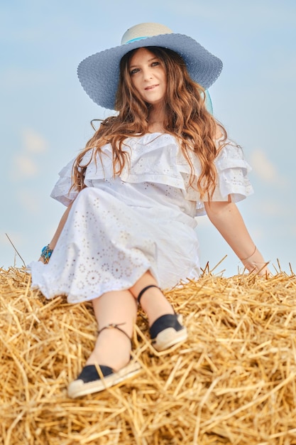 Zorgeloze vrouw zit op de top van hooiberg op het veld in zonnige dag