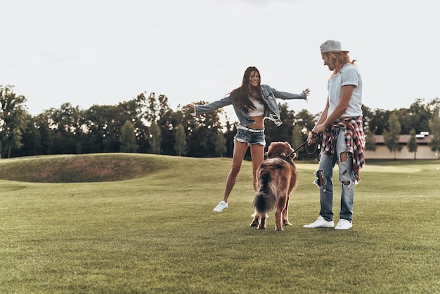 Zorgeloze zondag in het park. Volledige lengte van modern jong stel dat met hun hond speelt terwijl ze vrije tijd in het park doorbrengen